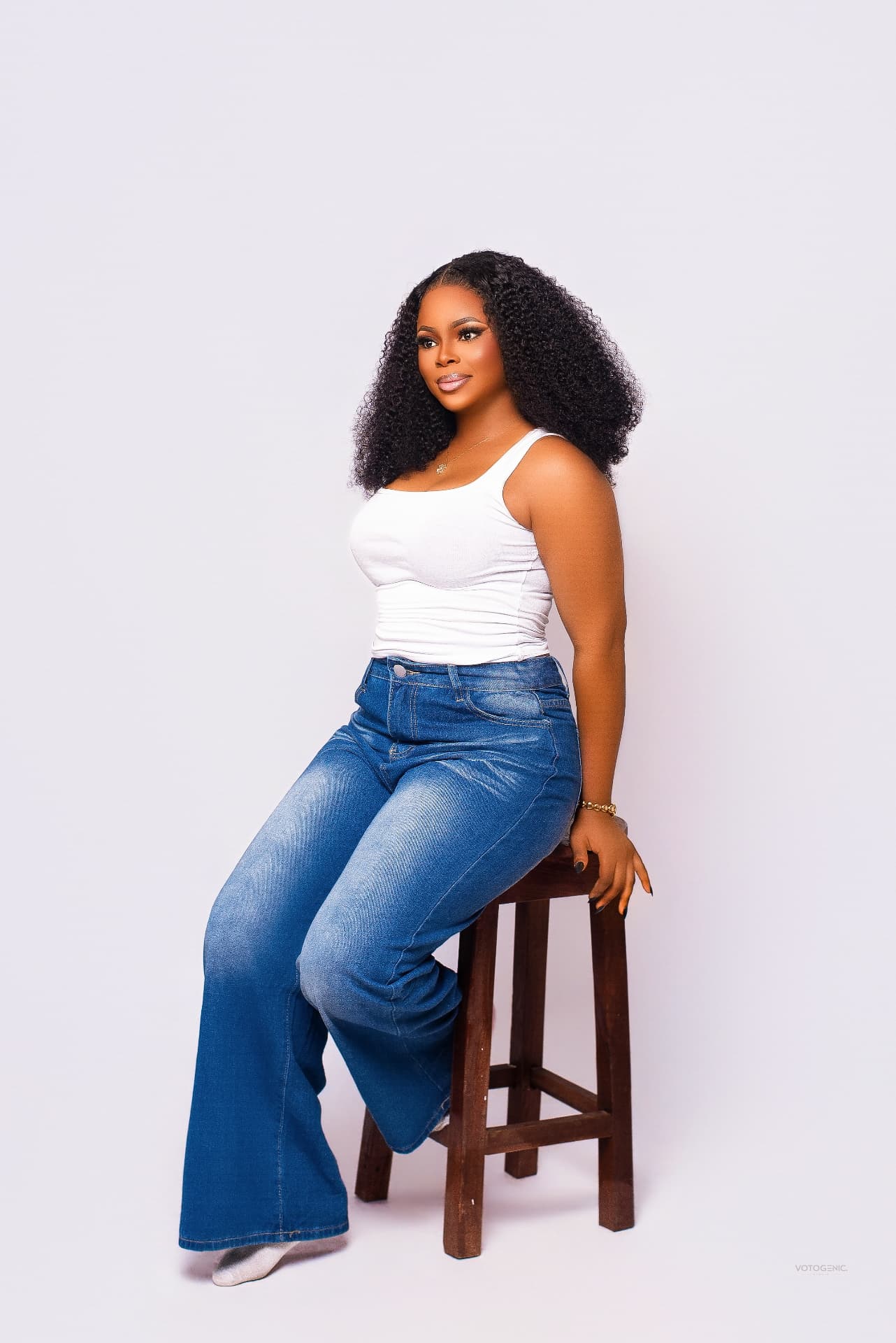 Model in white top and wide-leg denim seated on a stool